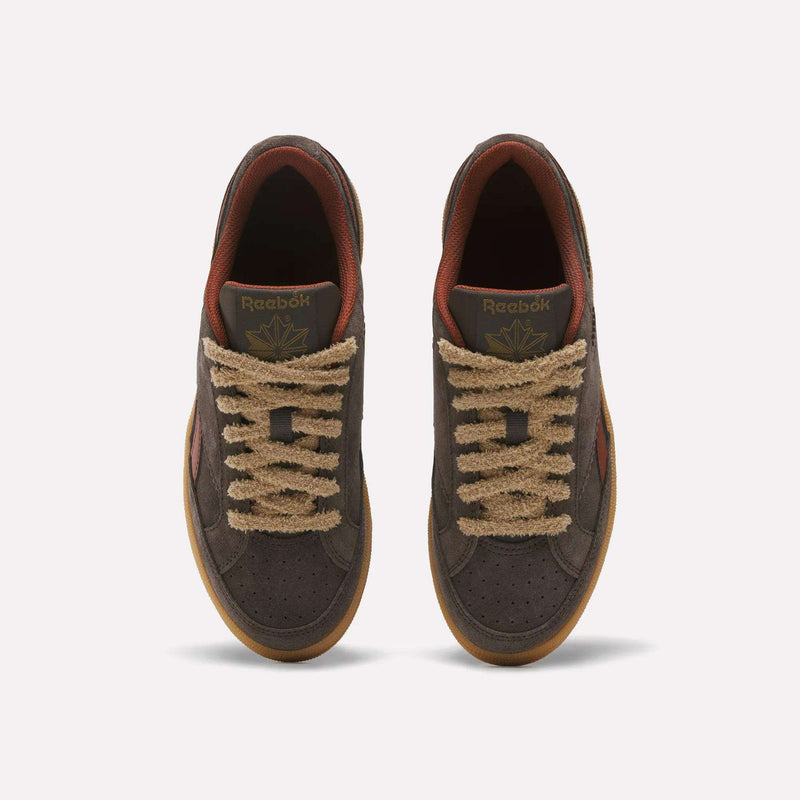 A pair of Reebok Women’s Club C Grounds 70 Shoes is shown from above against a plain white background. Featuring brown suede uppers, tan textured laces, gum soles, and a reddish-brown inner lining, these retro sneakers blend classic style with modern comfort.