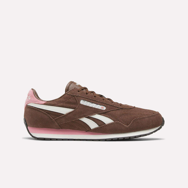 A pair of Women’s Classic AZ Shoes by Reebok is displayed in side profile on a plain light background, featuring a formal brown upper with chalk-white stripes and expressive pink accents on the heel and sole. These vintage-inspired sneakers seamlessly combine classic style with modern comfort, making them an excellent choice for women’s running shoes.