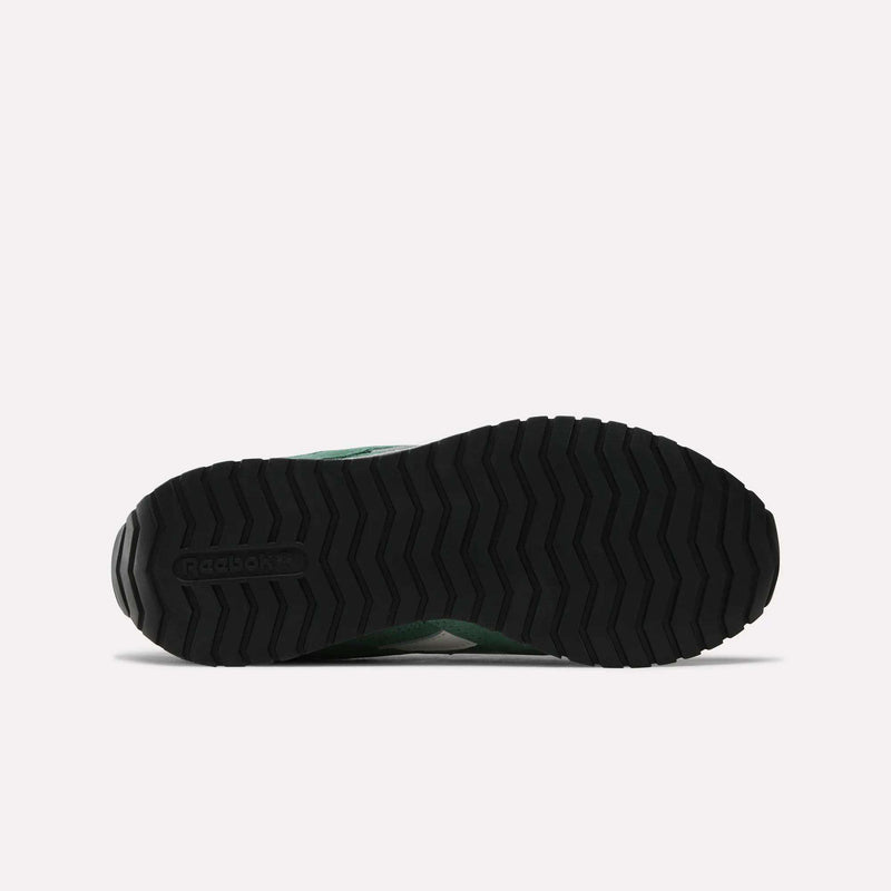 The image displays the black rubber outsole of the Reebok Women’s Classic AZ Shoes as seen from below, showcasing a zigzag tread pattern and the embossed Reebok logo near the heel—a subtle tribute to vintage sneakers and iconic women’s running shoes.