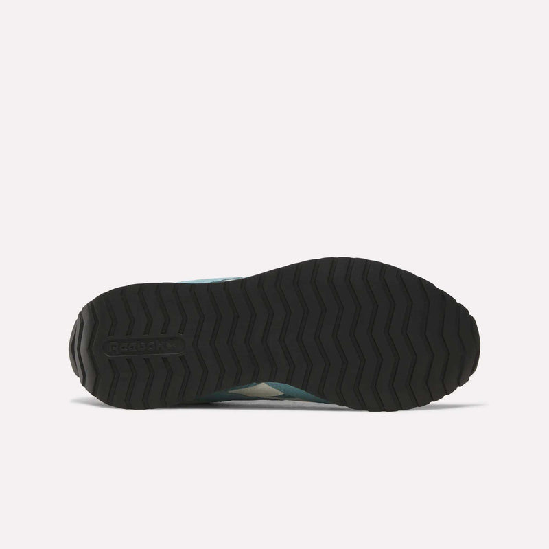The image displays the black rubber outsole of the Reebok Women’s Classic AZ Shoes, viewed from below, featuring a zigzag tread pattern and the Reebok logo embossed near the heel—an iconic detail characteristic of retro running shoes.