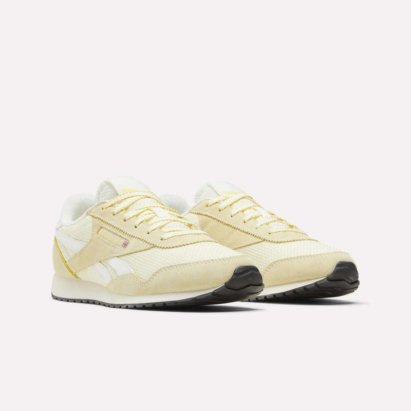 A pair of Reebok Women’s Classic AZ Shoes in beige and white with yellow accents, featuring a crochet textile upper, white laces, and black soles, are displayed on a plain white background.