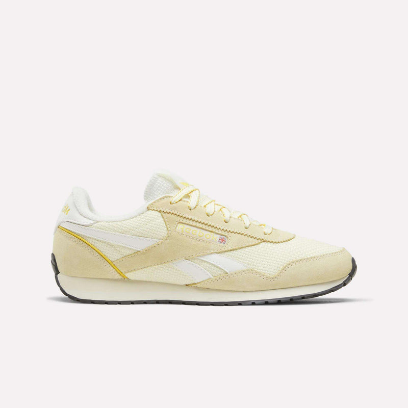 A side profile of the Reebok Women’s Classic AZ Shoes is displayed against a plain white background, showcasing their Raw Yellow/Athletic Gold/Chalk colorway. These sneakers feature a crochet textile upper for added texture, complemented by white accents, white laces, and a contrasting black sole.