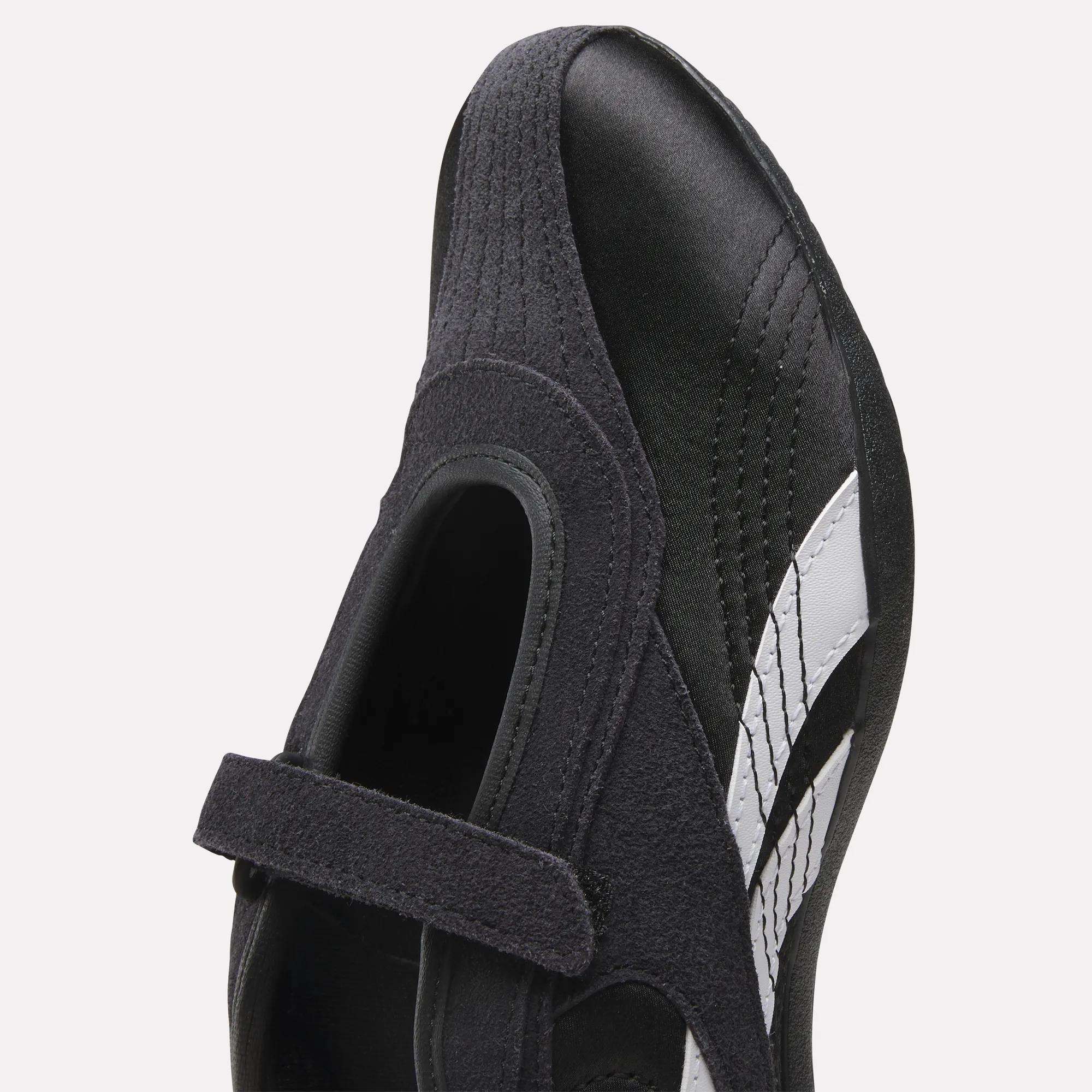 Close-up of Reebok Women's Ultra Lo Mary Jane Shoes, black low-profile design with a velcro strap, suede accents, and a white side stripe, viewed from above.