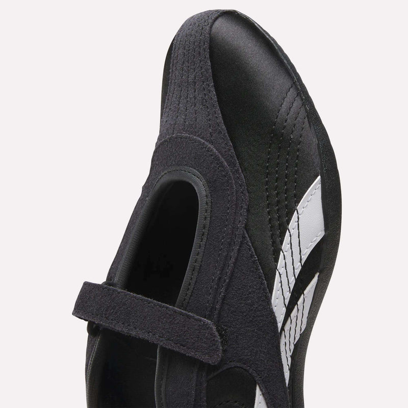 Close-up of Reebok Women's Ultra Lo Mary Jane Shoes, black low-profile design with a velcro strap, suede accents, and a white side stripe, viewed from above.