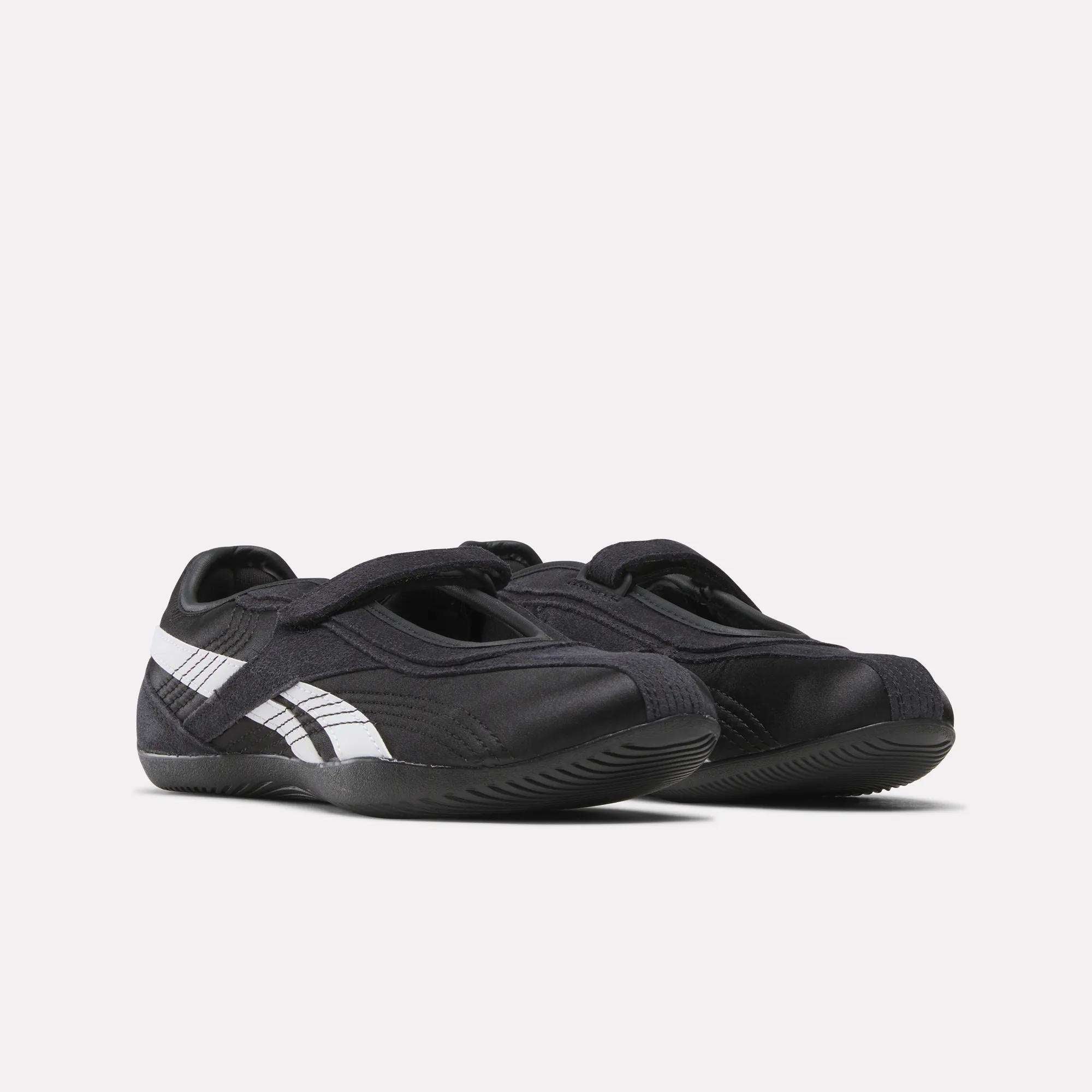 A pair of Women's Ultra Lo Mary Jane Shoes by Reebok, black with white stripes and Velcro straps, styled as low-profile runners and displayed side by side on a plain white background.