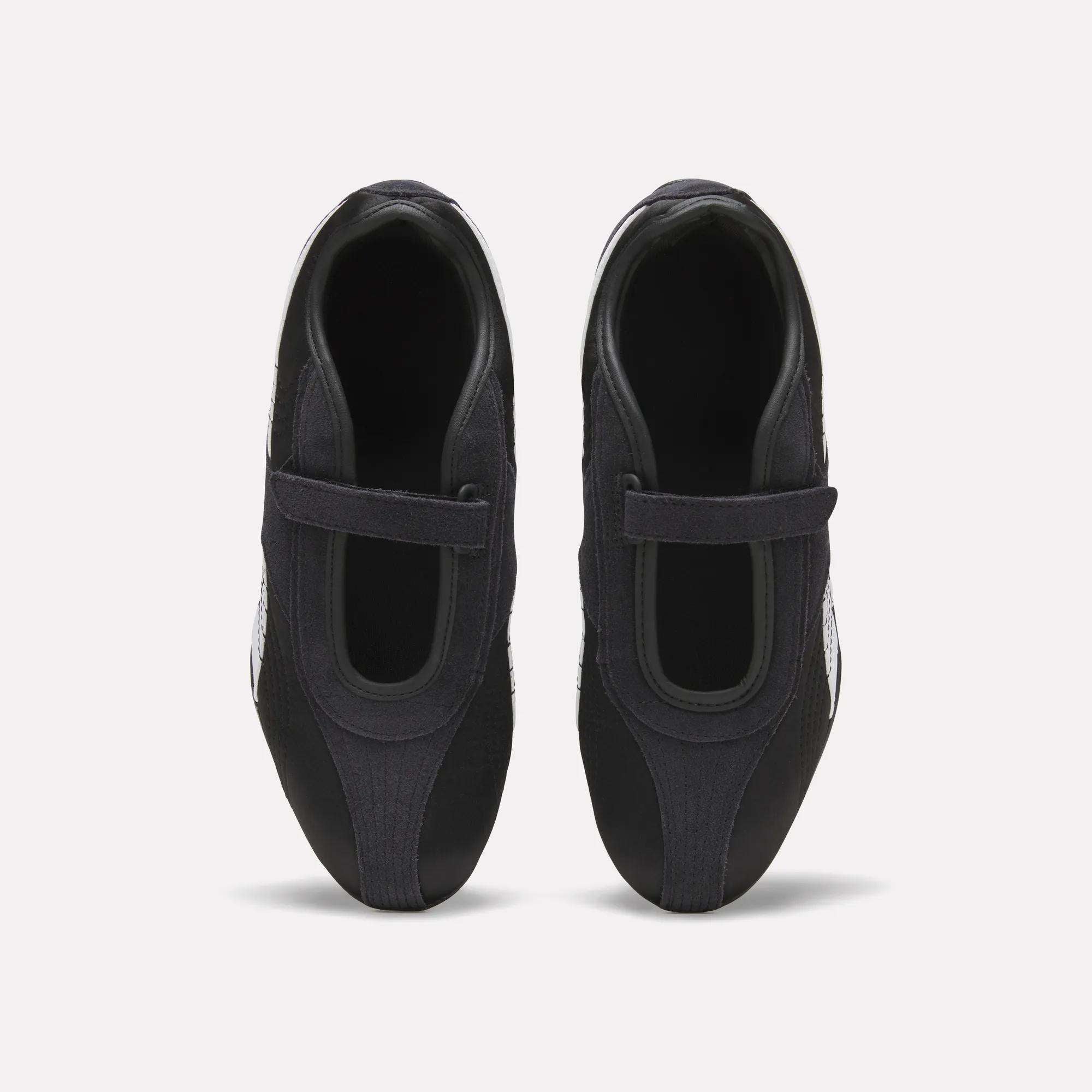 Top view of Reebok Women's Ultra Lo Mary Jane Shoes in black, featuring a single velcro strap on each, displayed side by side on a plain white background.