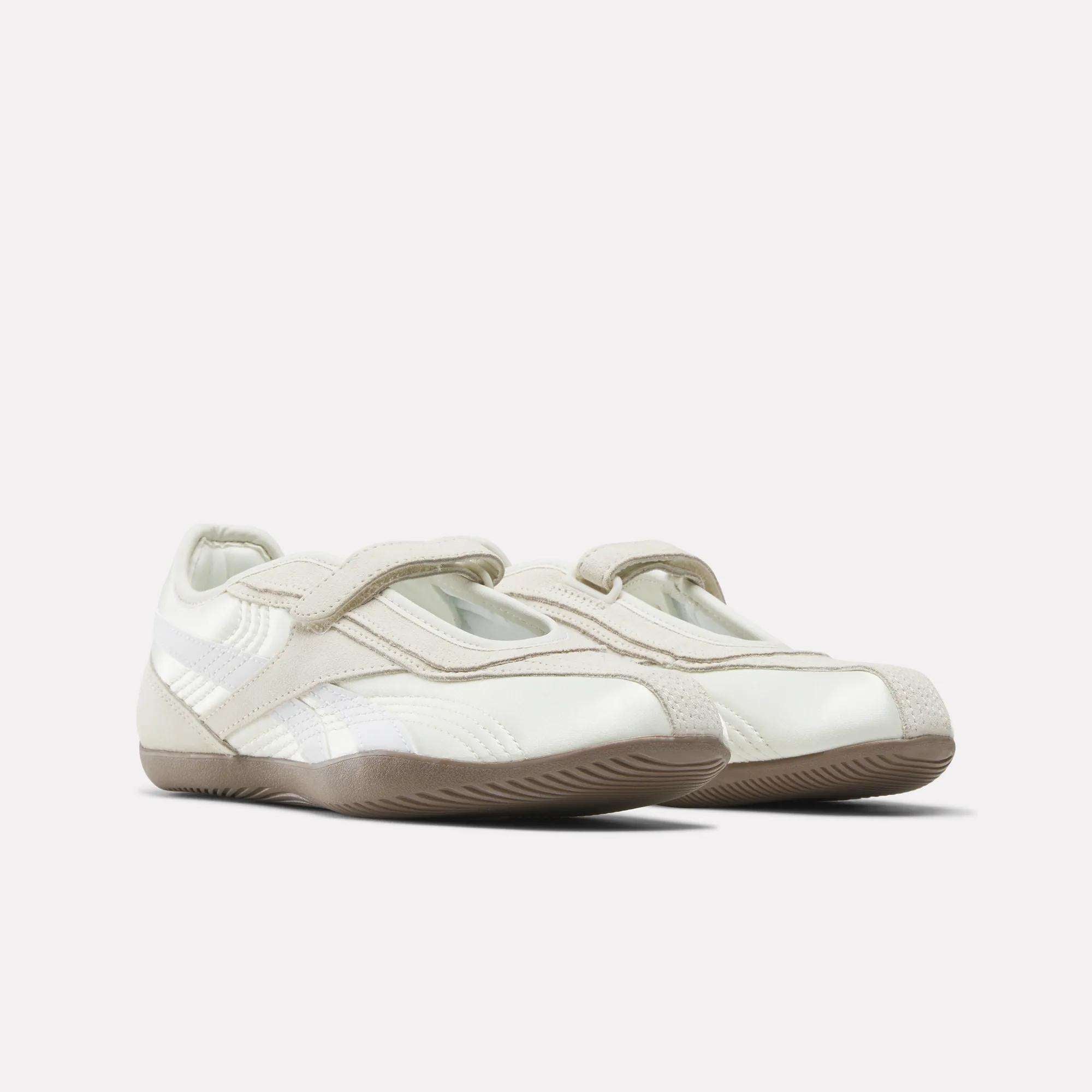 The Reebok Women's Ultra Lo Mary Jane Shoes feature a white and beige low-profile runner design with Velcro straps and subtle stitching details, displayed on a plain light background.