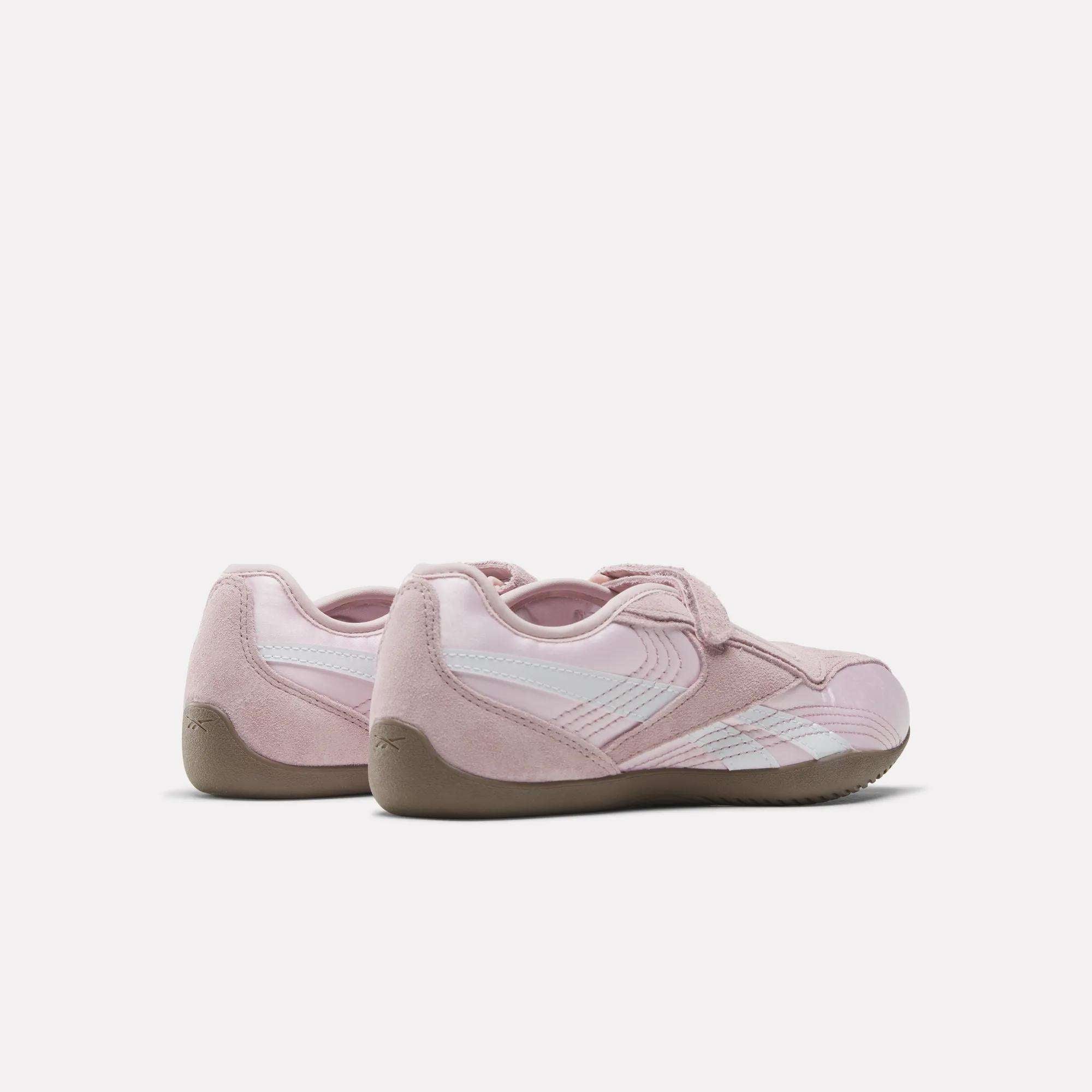The Reebok Women's Ultra Lo Mary Jane Shoes in pink, featuring white stripes and gum soles, display a sleek low-profile design from back and side views against a plain white background.