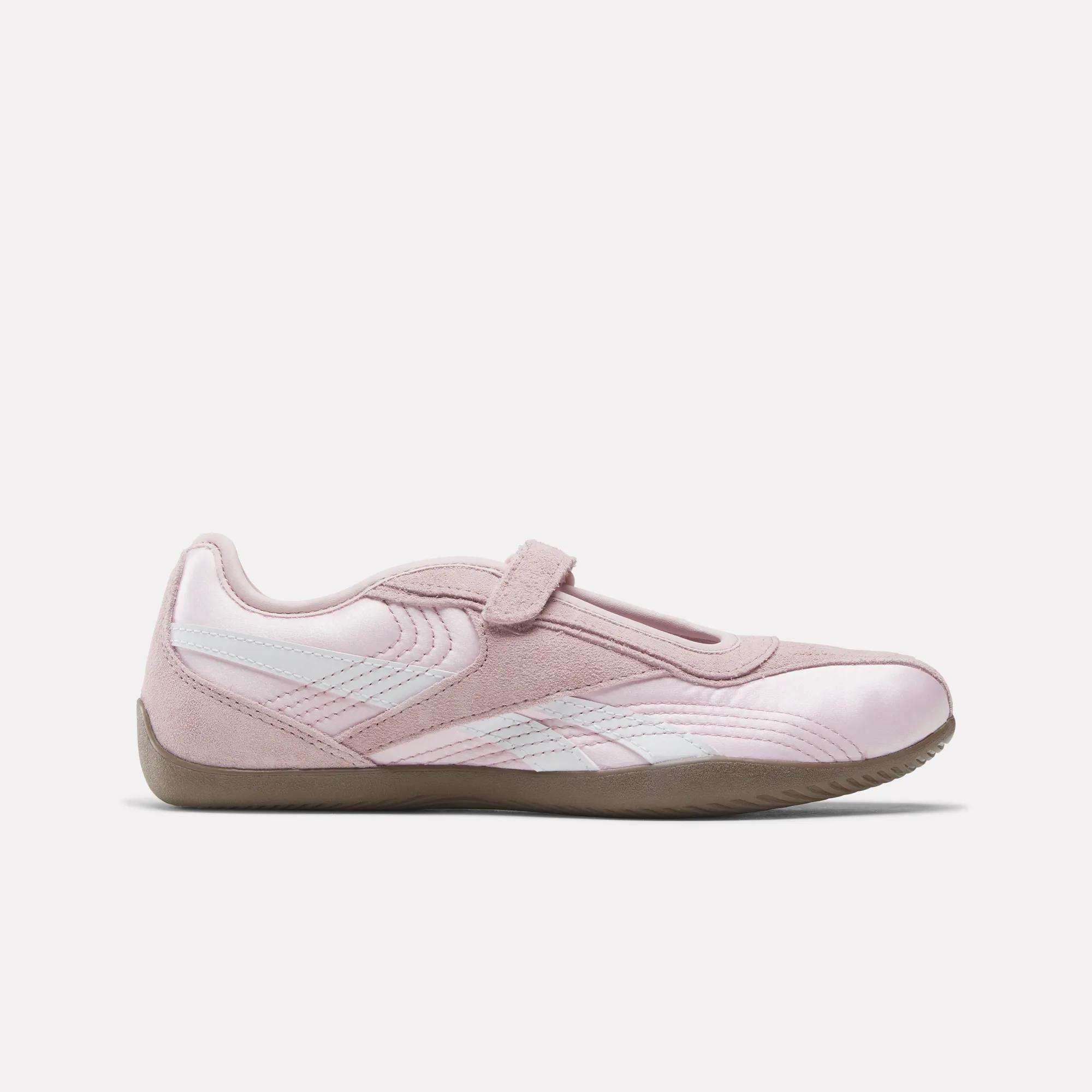 The Reebok Women's Ultra Lo Mary Jane Shoes are light pink with white accents, a suede finish, velcro strap, and tan rubber sole, shown in profile on a plain white background.