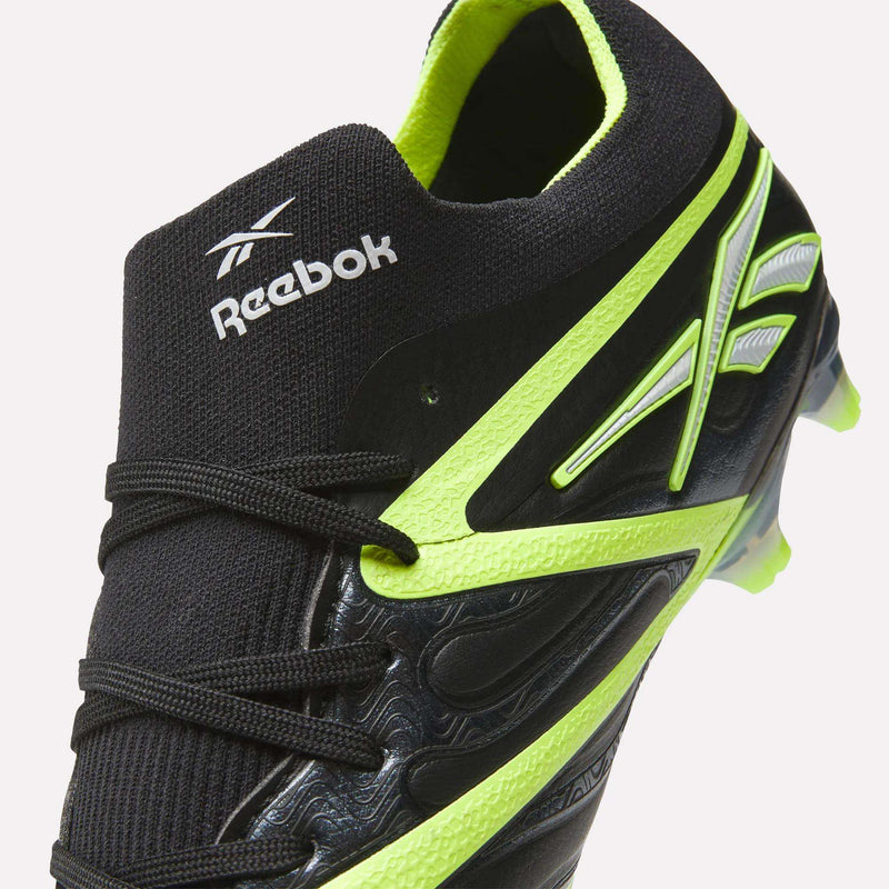 Close-up of Reebok Sidewinder 26 Elite FG Cleats in black with neon yellow accents and laces, engineered for firm ground play and improved ball control, showing the Reebok logo on the tongue and side.