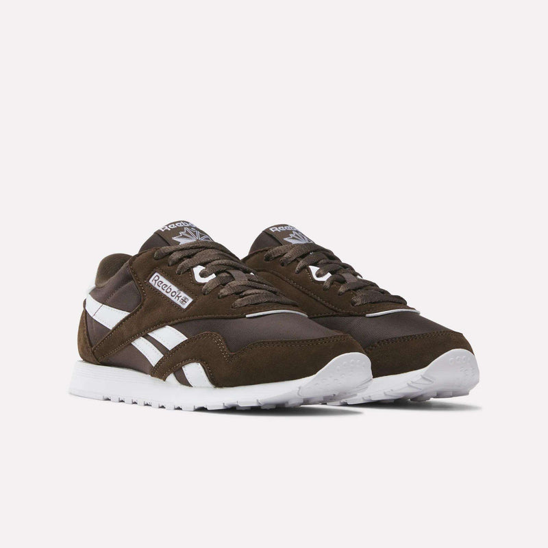 A pair of Women’s Classic Nylon Shoes by Reebok, featuring a brown colorway with white soles and signature white side stripes, is displayed on a plain white background and exemplifies vintage style with timeless appeal.