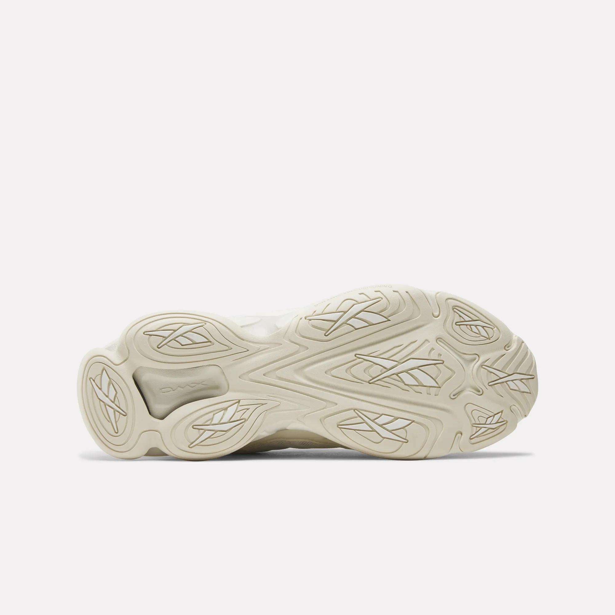 The image displays the outsole of Reebok's DMX Series 3000 Shoes facing up, in light beige with wavy and geometric tread patterns for grip. The intricate design emphasizes comfort, with visible adiPRENE branding on one section.