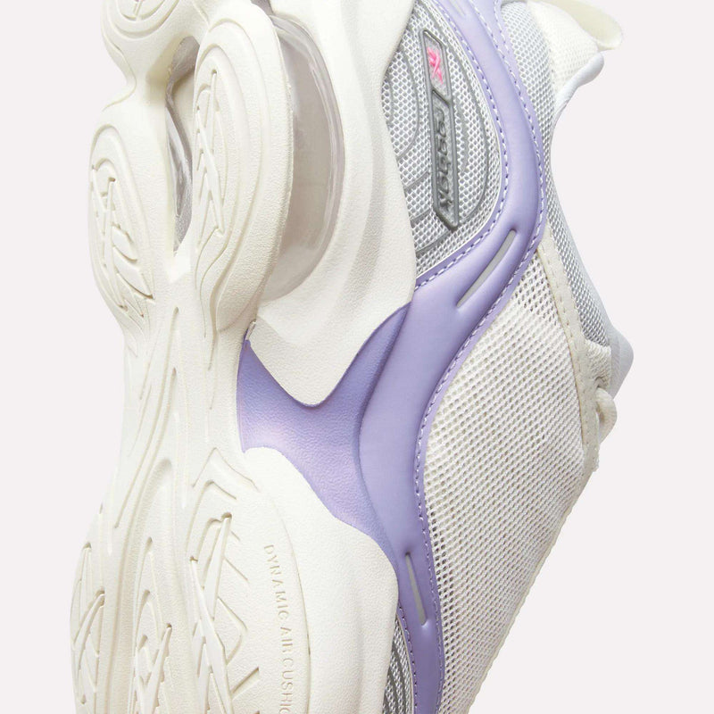 A close-up of the Reebok Women’s DMX Series 3000 Shoes highlights the textured white sole, mesh upper, and a purple accent. This sneaker showcases gray and silver details with a modern, chunky design, enhanced by Reebok’s DMX moving air technology for lightweight support.