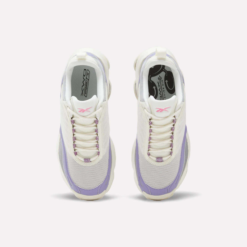 A pair of Women’s DMX Series 3000 Shoes by Reebok in white with purple accents is shown from above. The sneakers feature mesh toe boxes, white laces, pink Reebok logos on the tongues, and purple eyelets. Their chunky, light-colored soles utilize DMX moving air technology for ultra-cushioned comfort and lightweight support with every step.
