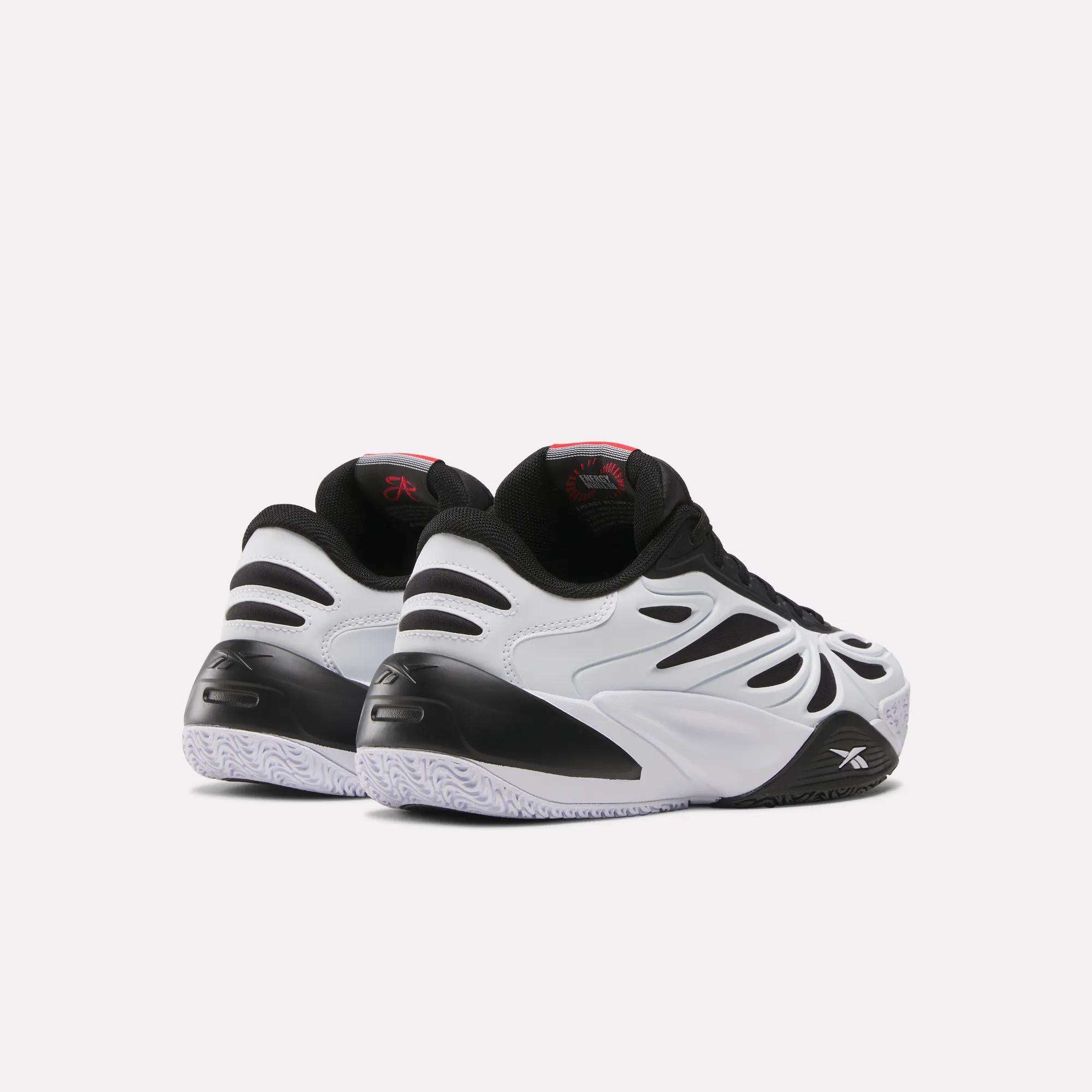 The Reebok Angel Reese 1 Shoes for big kids, featuring black and white wavy designs, black accents, and textured white soles, are displayed from the back and side on a plain light background.