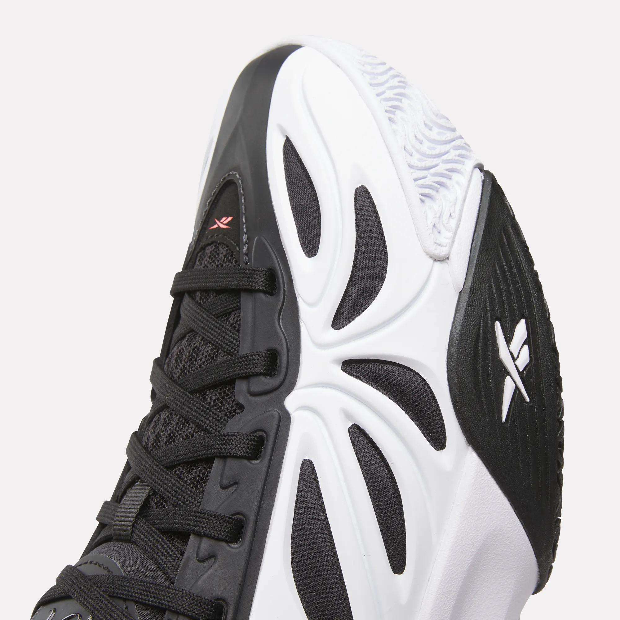 Close-up of the toe and side of the Reebok Angel Reese 1 Shoes - Big Kids, a black and white performance basketball sneaker with a textured sole, geometric design, black laces, and two white logos inspired by Angel Reese.