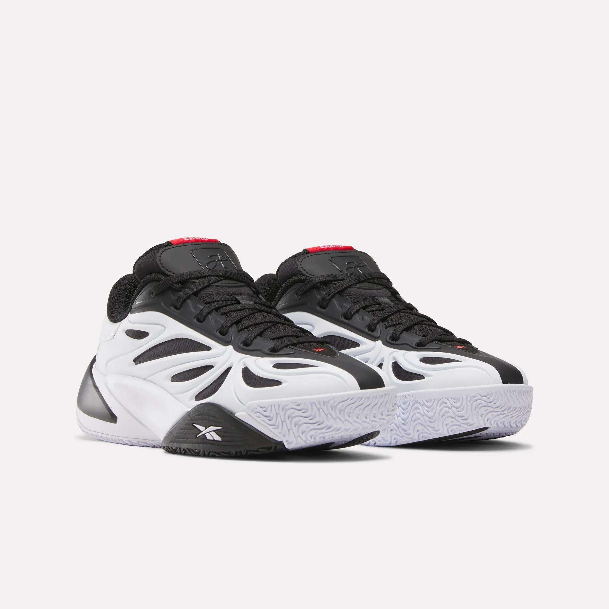 The Reebok Angel Reese 1 Shoes - Big Kids feature a bold, futuristic black and white design with black accents, a chunky sole, and red tongue details, inspired by Angel Reese shoes and displayed on a plain white background.