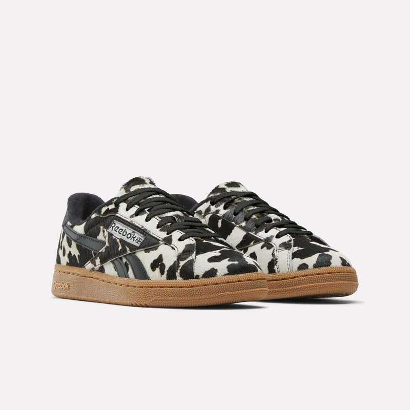 Reebok Women's Club C Grounds UK Shoes feature a bold black and white cow print, black accents, and light brown gum soles—perfect for anyone seeking unique women's footwear. Displayed on a plain white background.