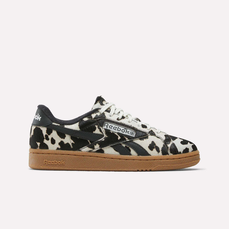 Women's Club C Grounds UK Shoes by Reebok feature a bold black and white cow print upper, white laces, black accents, and a brown gum sole, displayed on a plain white background.