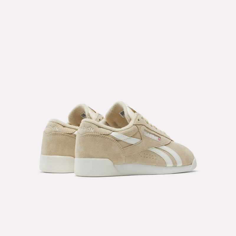The Reebok Women's Freestyle Lo Shoes feature beige suede uppers, white side stripes, and rubber soles, shown from the back and side on a plain white background.