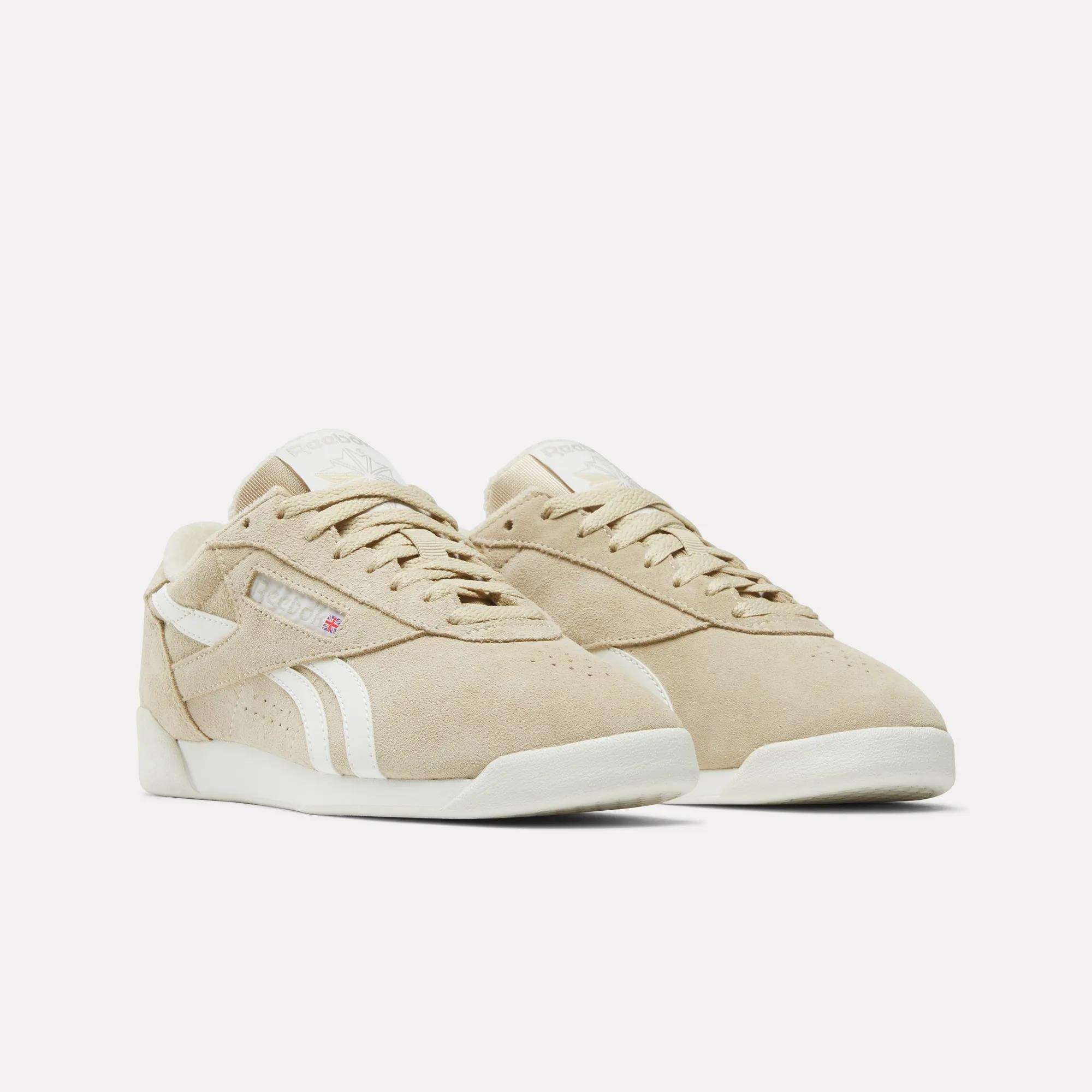 Reebok Women's Freestyle Lo Shoes in beige suede with white accents, white soles, and classic side stripes—retro sneakers ideal for everyday style.