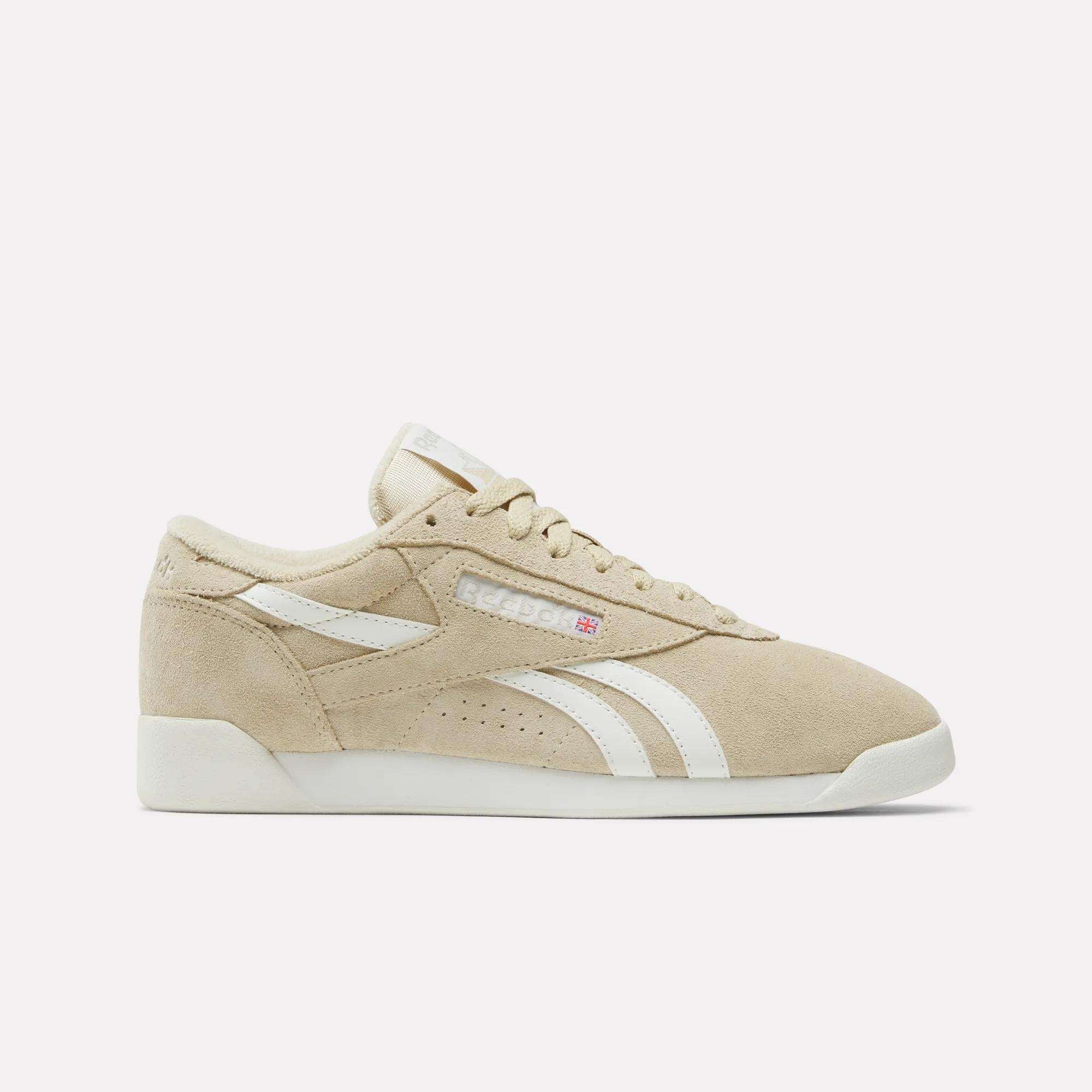 The Women's Freestyle Lo Shoes by Reebok feature beige suede, white stripes, a white sole, and beige laces. Displayed in a side profile on a plain white background, they capture the classic retro sneaker style.