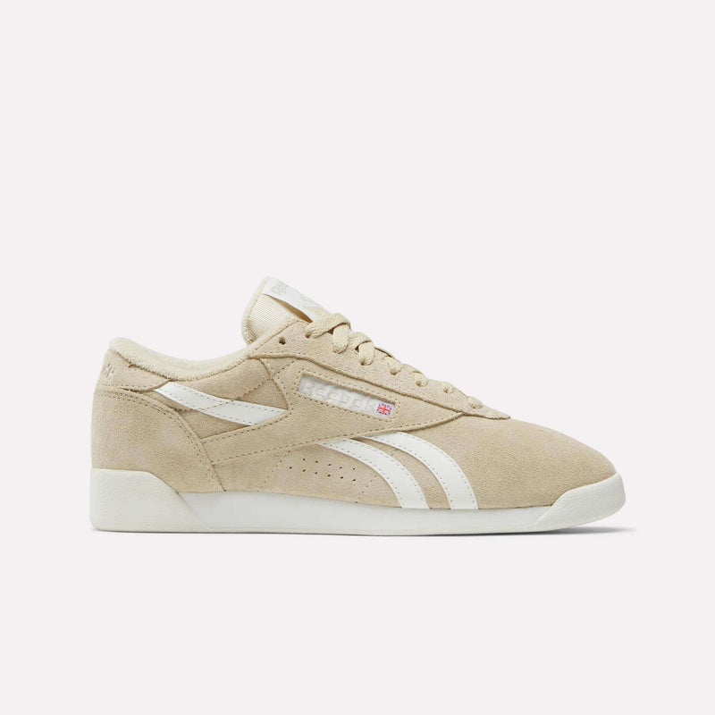 The Women's Freestyle Lo Shoes by Reebok feature beige suede, white stripes, a white sole, and beige laces. Displayed in a side profile on a plain white background, they capture the classic retro sneaker style.