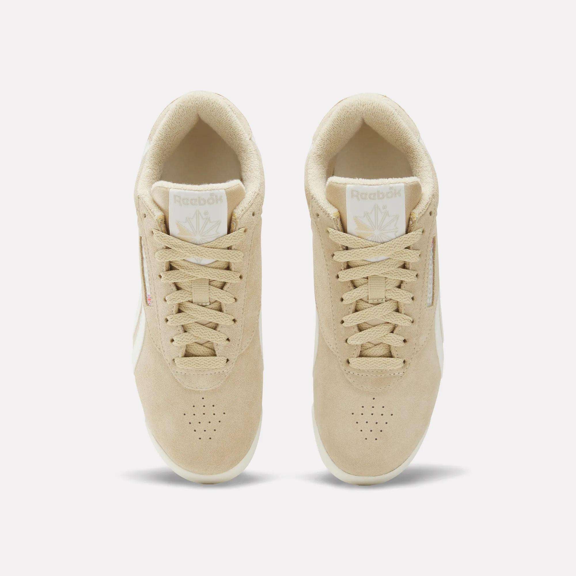 Top view of a pair of Women's Freestyle Lo Shoes by Reebok in beige with white soles and beige laces, featuring the Reebok logo on the tongue and side. The sneakers are placed side by side on a plain white background.