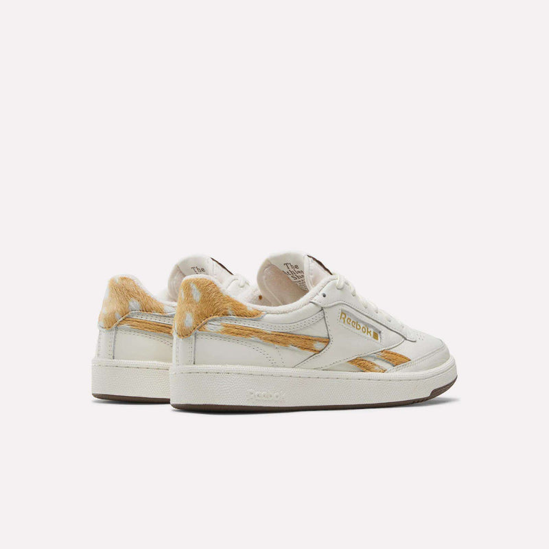 Two white Reebok Club C Revenge Vintage Shoes feature a leather upper with tan fur accents on the heel and side, gold Reebok branding, and a classic low-cut silhouette that exudes vintage style—all set against a plain white background.