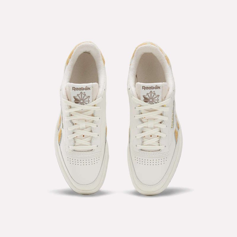 Top view of a pair of Reebok Club C Revenge Vintage Shoes with beige accents, white laces, and perforated detailing on the toes, featuring a classic leather upper. These tennis-inspired sneakers are displayed on a plain light background.