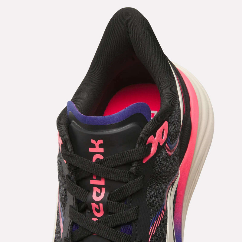 Top view of Reebok Women's Viva Speed Shoes in black with pink, purple, and white accents, black laces, and "Reebok" in pink on the tongue. The white sole features a pink gradient on the side and offers extra cushioning for all-day comfort.