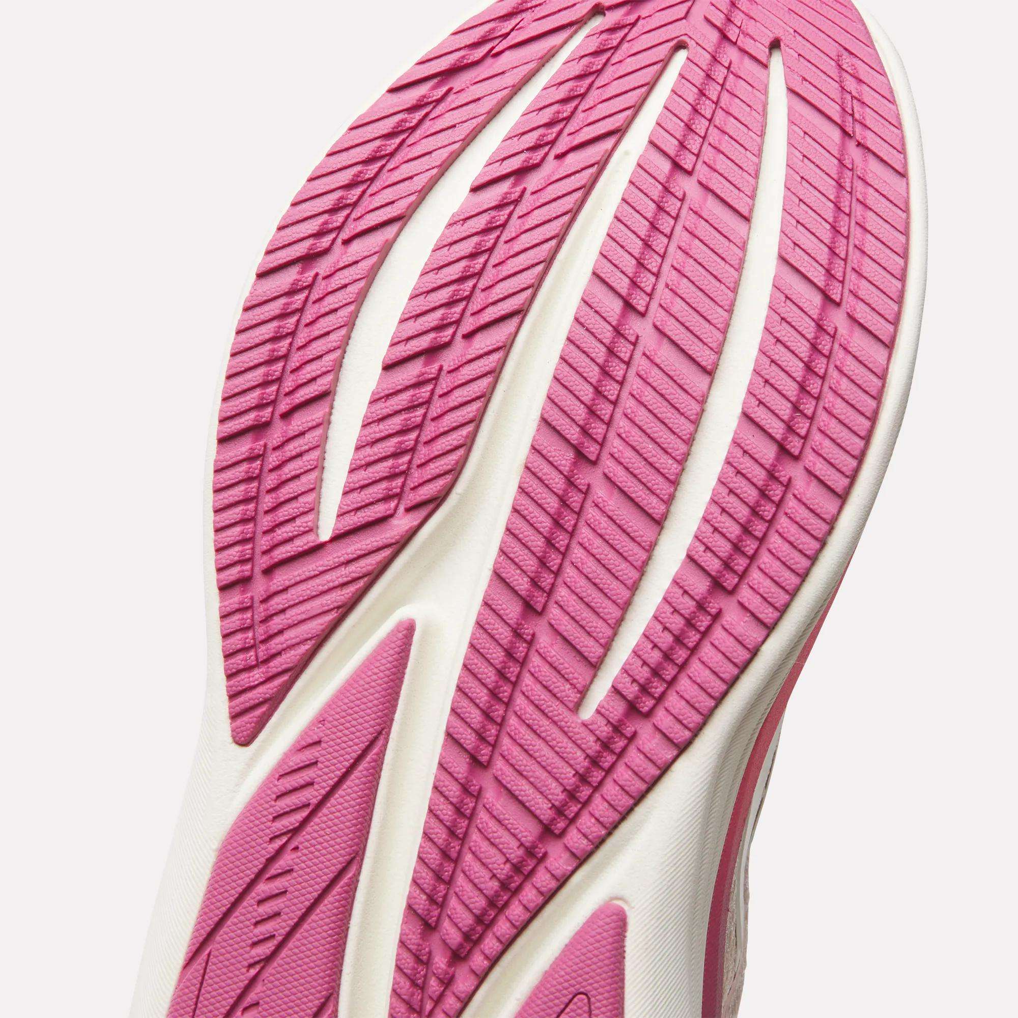 Close-up of the pink and white sole of Reebok Women's Viva Speed Shoes, showing textured grip with deep grooves and diagonal lines against a white background—highlighting features of these cushioned sneakers.