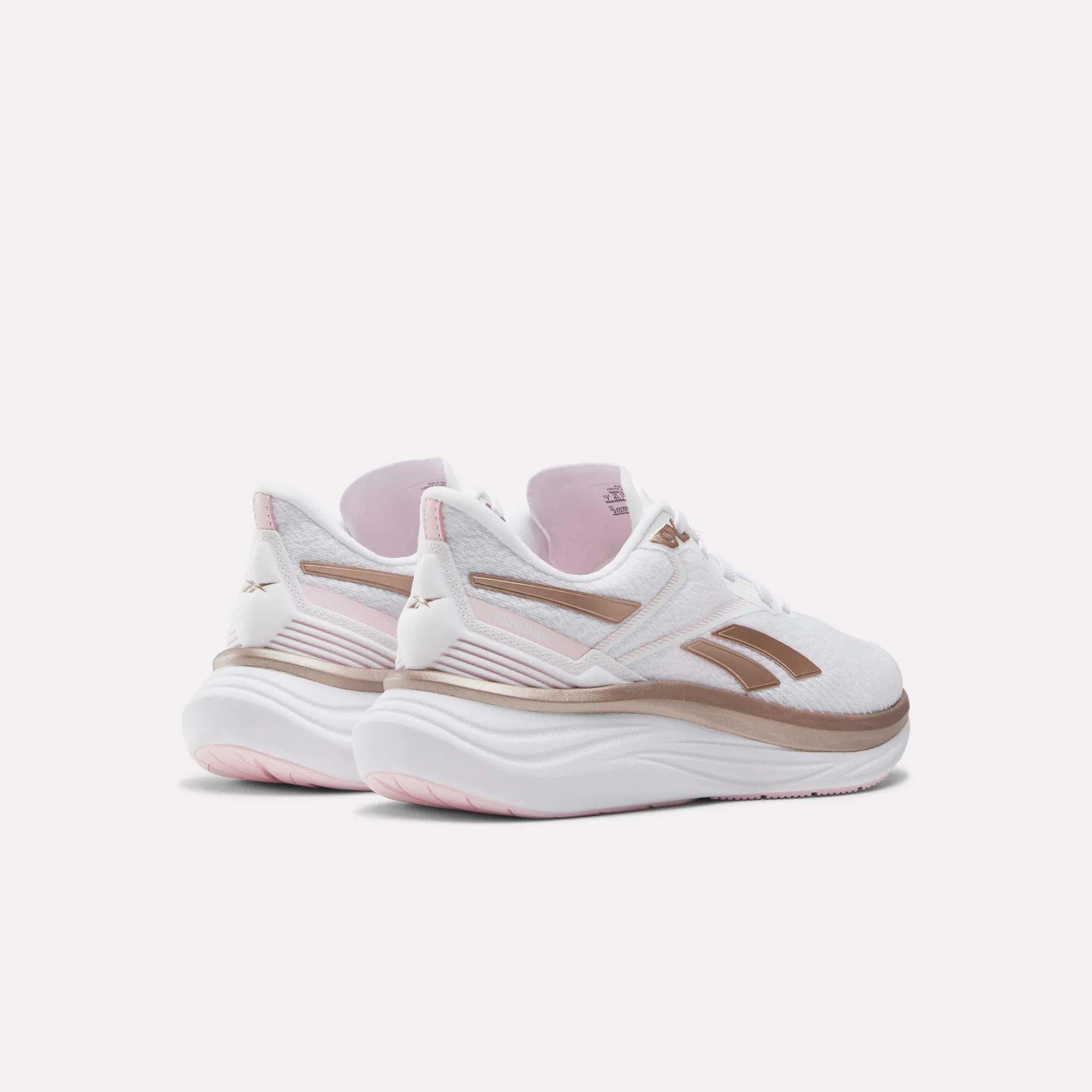 The Women's Viva Speed Shoes by Reebok feature a white design with light pink and bronze accents, thick cushioned soles, and the Reebok logo on the heel, shown against a light background.