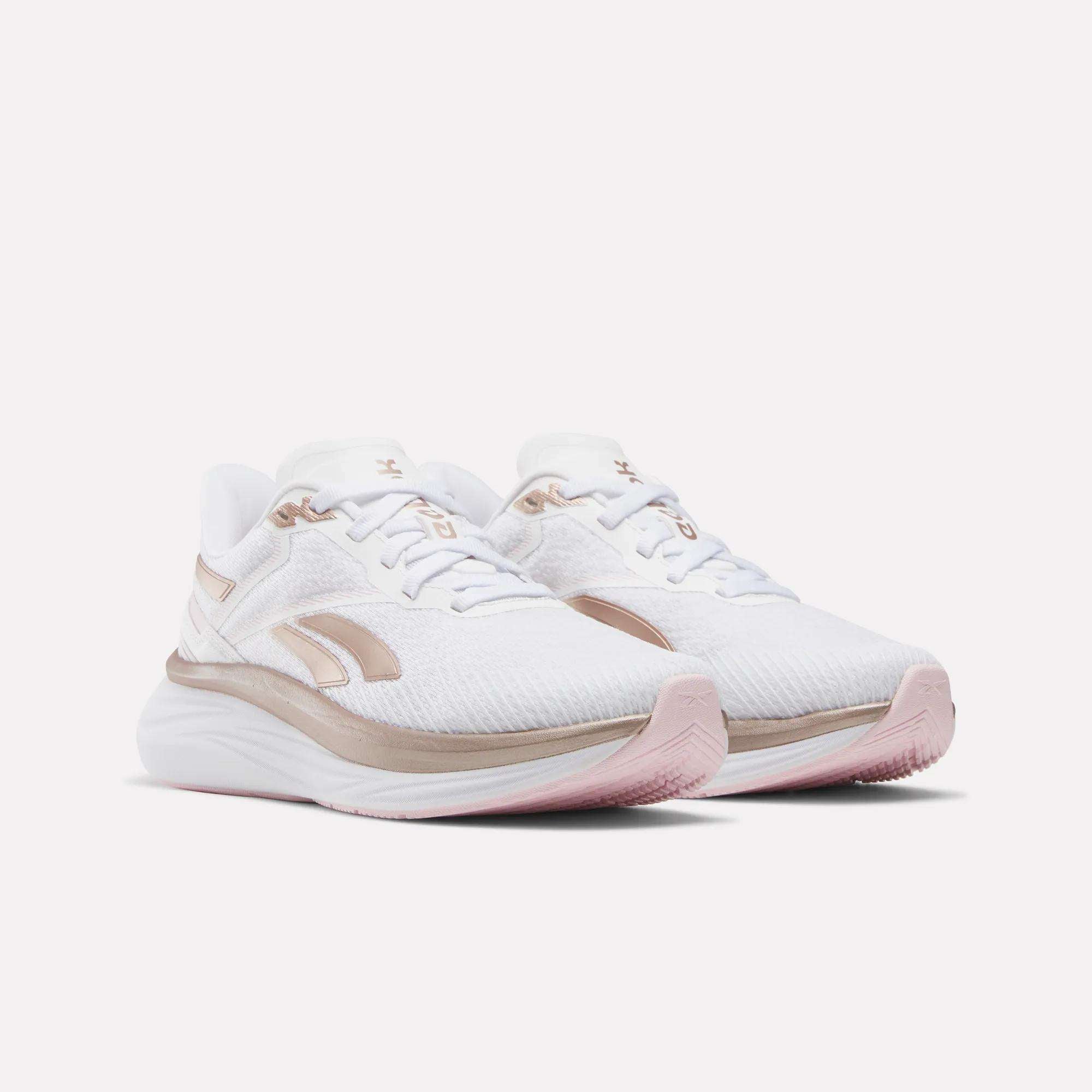The Reebok Women's Viva Speed Shoes are white with light pink and beige accents, featuring a textured breathable upper, cushioned sole, and subtle branding. They are displayed side by side at a slight angle.