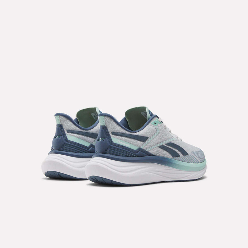 The Reebok Women's Viva Speed Shoes in light gray feature teal and navy blue accents, cushioned thick white soles, and dark outsoles, displayed angled from the back against a plain white background.