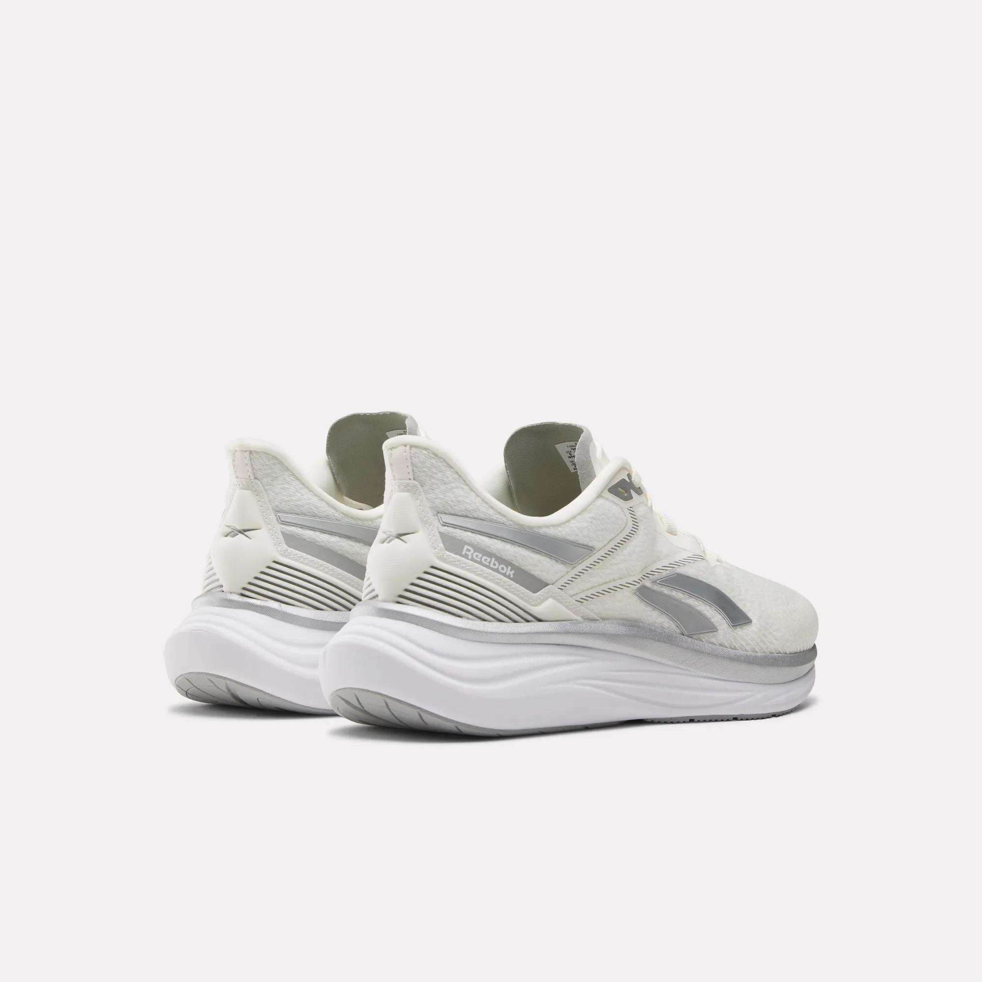 A pair of Reebok Men's Viva Speed Shoes in white, featuring thick curved soles and extra cushioning, is displayed from a rear three-quarter view against a plain light background.