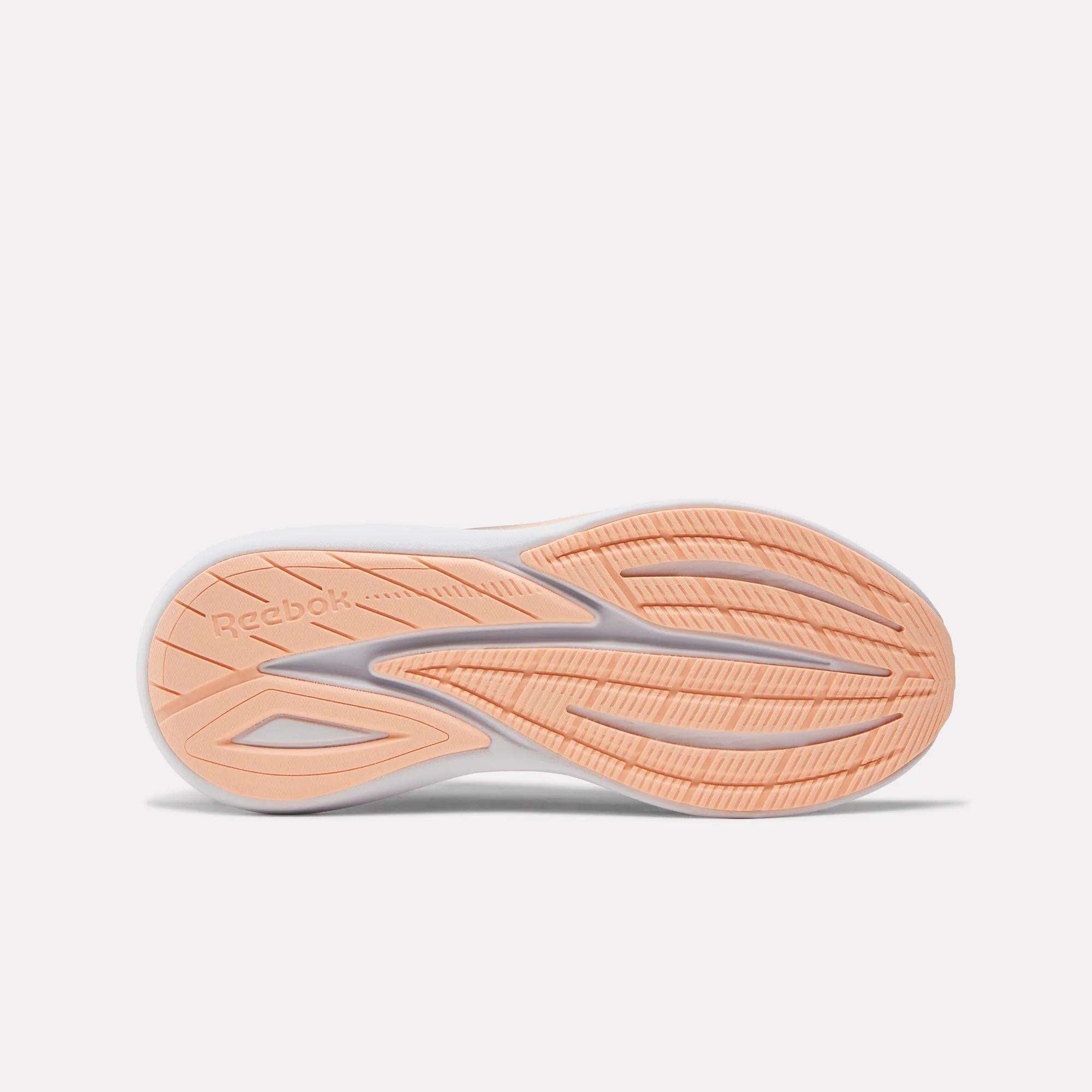 The image shows the sole of the Women's Viva Speed Shoes by Reebok. The peach-colored sole with white accents has extra cushioning, a patterned grip, and features the Reebok logo on the left side.