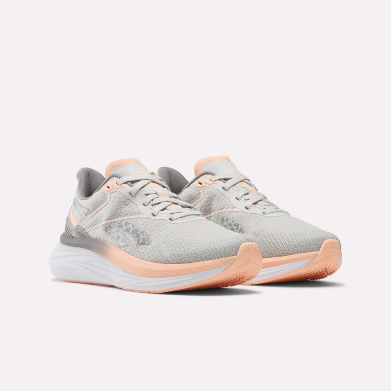 The Reebok Women's Viva Speed Shoes feature a light gray design with peach and white accents, extra cushioning for comfort, and a lace-up closure, shown on a plain white background.