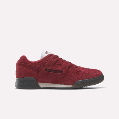 The Reebok Workout Plus Shoes in red suede, with black soles and laces plus a white tongue, are shown in side profile on a white background, highlighting their classic '80s-inspired workout shoe style.