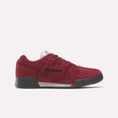 The Reebok Workout Plus Shoes in red suede, with black soles and laces plus a white tongue, are shown in side profile on a white background, highlighting their classic '80s-inspired workout shoe style.