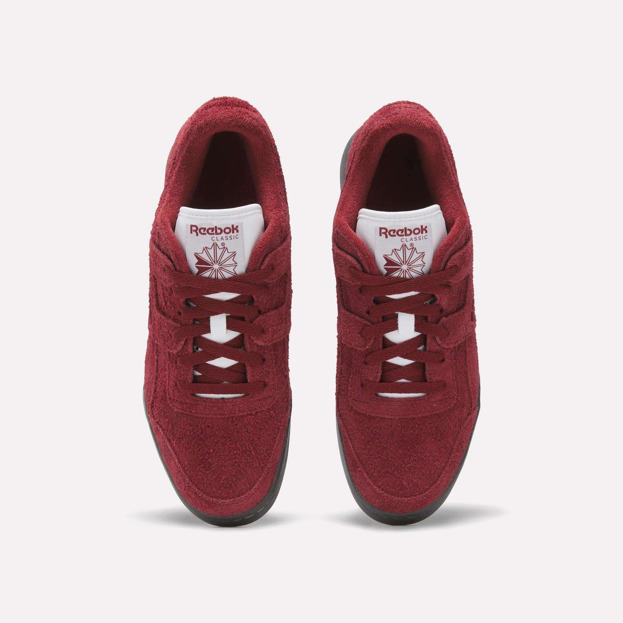 A pair of red Reebok Workout Plus Shoes with white tongues, black soles, and matching red laces and logos is shown from above on a plain white background, highlighting the classic fitness style.