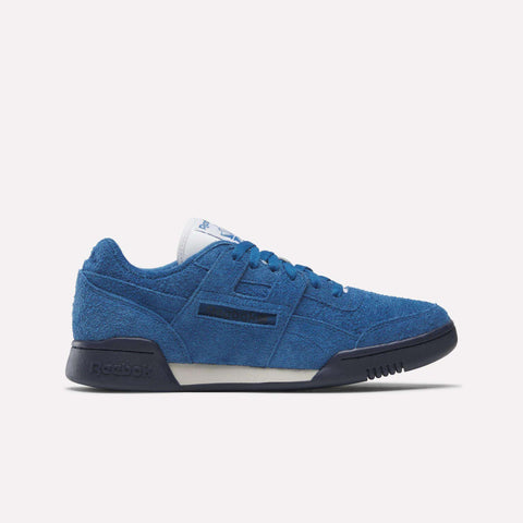 The Reebok Workout Plus Shoes feature blue suede uppers, a white tongue, navy blue sole, and subtle side branding, delivering classic workout style against a plain white background.