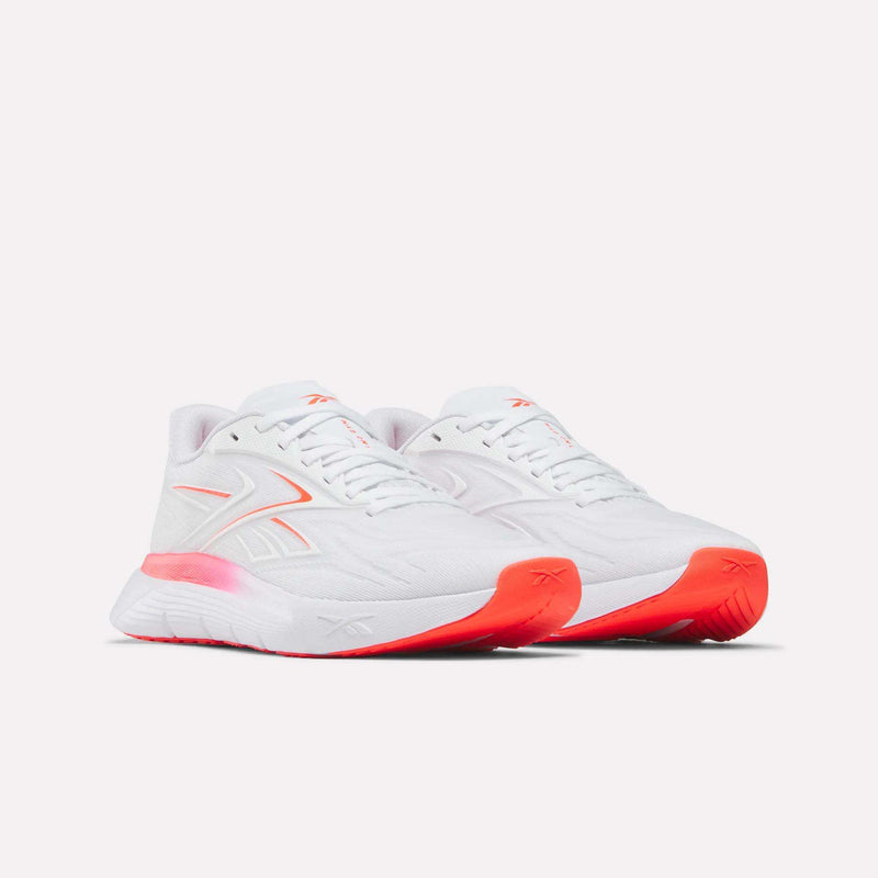 The Women's Nano Gym 2.0 Training Shoes by Reebok feature a low-top, white athletic design with light pink details and orange accents on the midsole and outsole, shown against a plain light background.