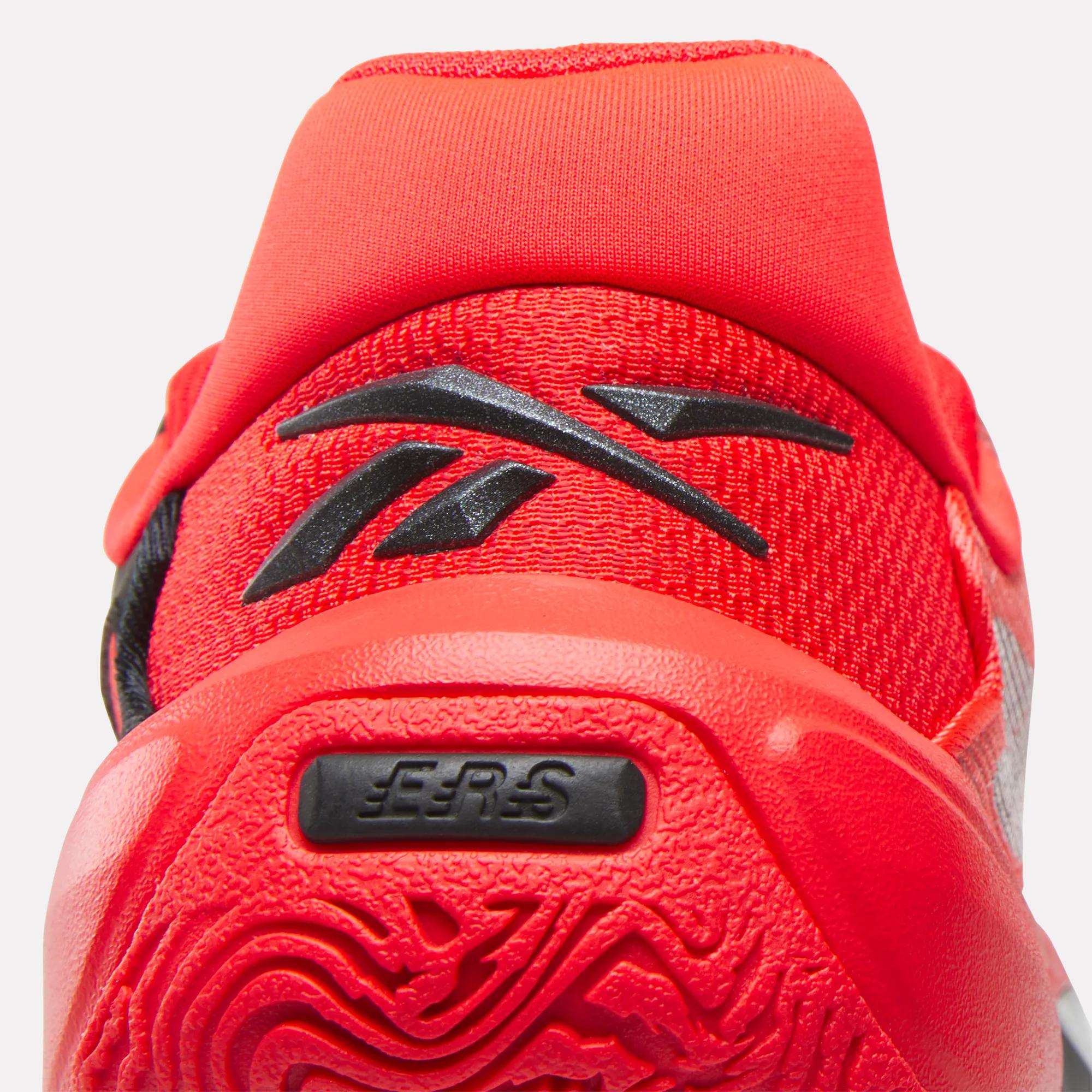 Close-up of the heel of a bright red Reebok Engine A 26 basketball shoe, showing the black logo, textured sole for stability, EER5 branding on the heel, and mesh upper material.
