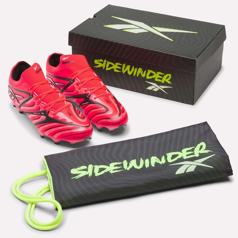 A pair of Reebok Sidewinder 26 Elite Firm Ground Cleats in bright red with black accents—engineered for excellent ball control on firm grass surfaces—accompanied by a shoe box and a black shoe bag featuring “SIDEWINDER” in green text, all displayed against a white background.