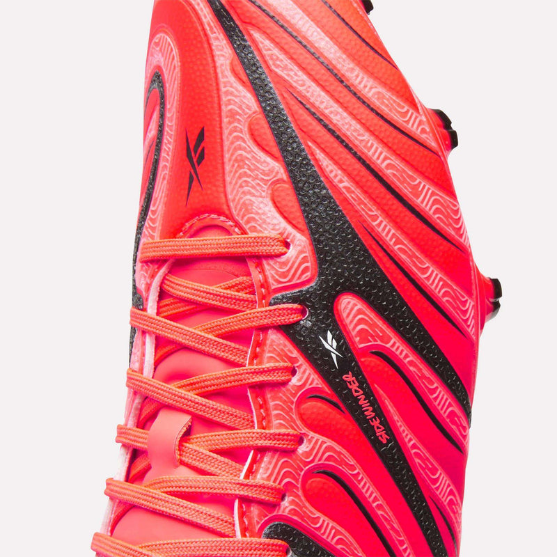Close-up of a bright red Reebok Sidewinder 26 Pro Firm Ground Cleat with black accents and a marbled pattern.