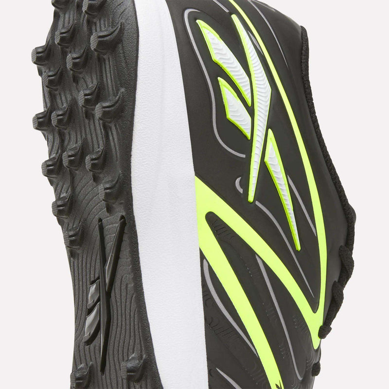 Close-up of the Reebok Sidewinder 26 League Turf Cleats, a black and white athletic soccer shoe with neon yellow accents designed specifically for turf players. The image highlights the textured sole, ideal for artificial soccer fields, and part of the upper, which features a striking stylized design.