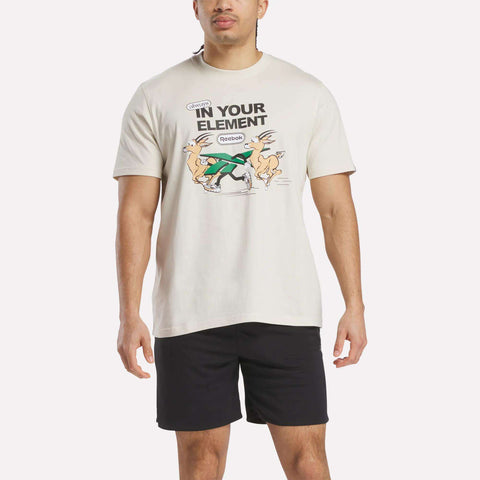 A man wears a Reebok Men's Club Graphic T-Shirt with cartoon animals and "IN YOUR ELEMENT" text, made from 100% cotton, paired with black shorts against a plain background.