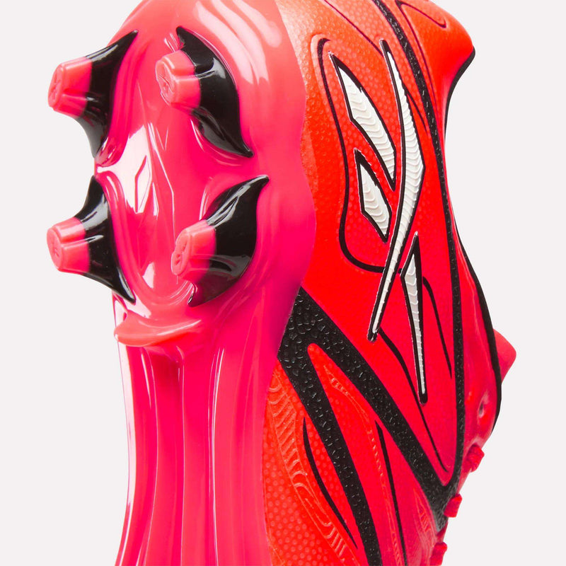 Close-up of the sole and heel area of the Reebok Sidewinder 26 League Firm Ground Cleats for big kids, showcasing brightly colored pink and black firm ground studs with white and orange design patterns.