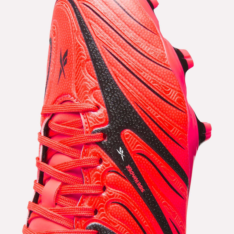Close-up of the Reebok Sidewinder 26 League Firm Ground Cleats for big kids in bright red and black, highlighting the textured patterns, laces, and firm ground studs with the Reebok logo visible on the side.